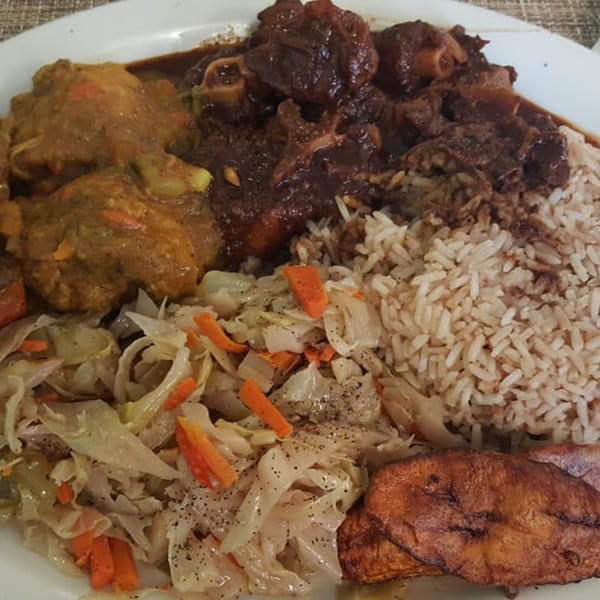 A plate of Sunshine Jamaican Restaurant's oxtail, curry chicken, rice and peas, steamed cabbage, and plantains.