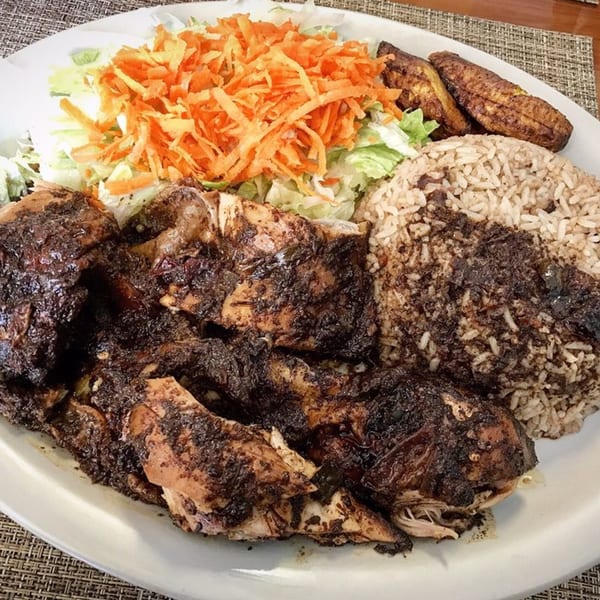 A plate of Jamaican jerk chicken, rice and peas, fried plantains, and a side salad.