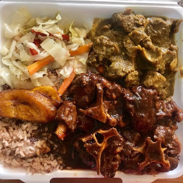 A takeout container with Jamaican oxtail, curry goat, rice and peas, steamed cabbage, and plantains.