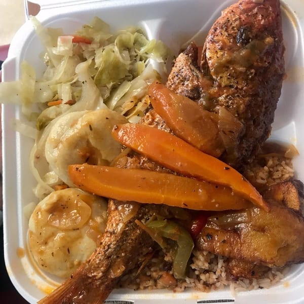 A takeout container filled with Jamaican brown stew fish, rice, steamed cabbage, carrots, and dumplings.